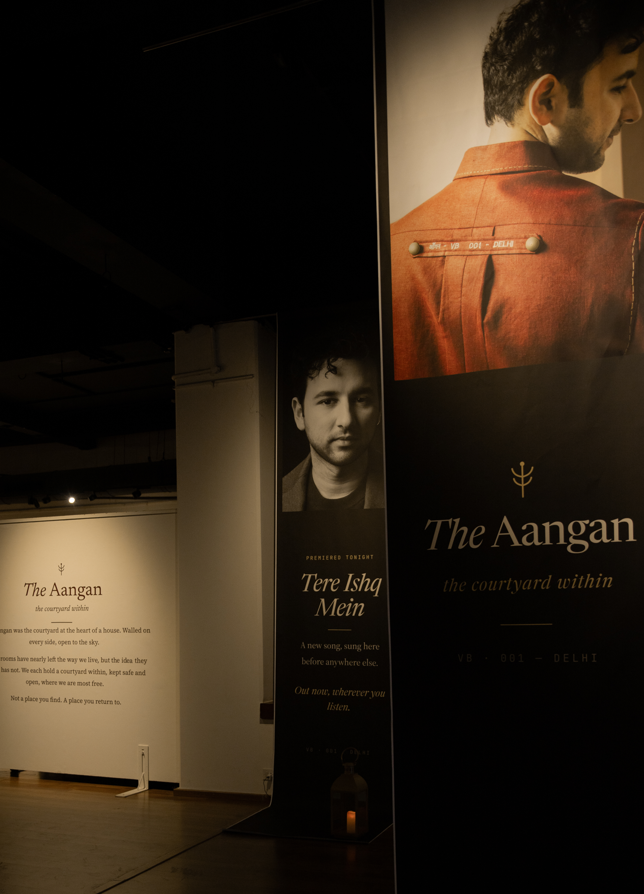 Gallery installation for The Aangan and the 2026 catalogue, banners, lanterns, and display panels in warm tungsten light.