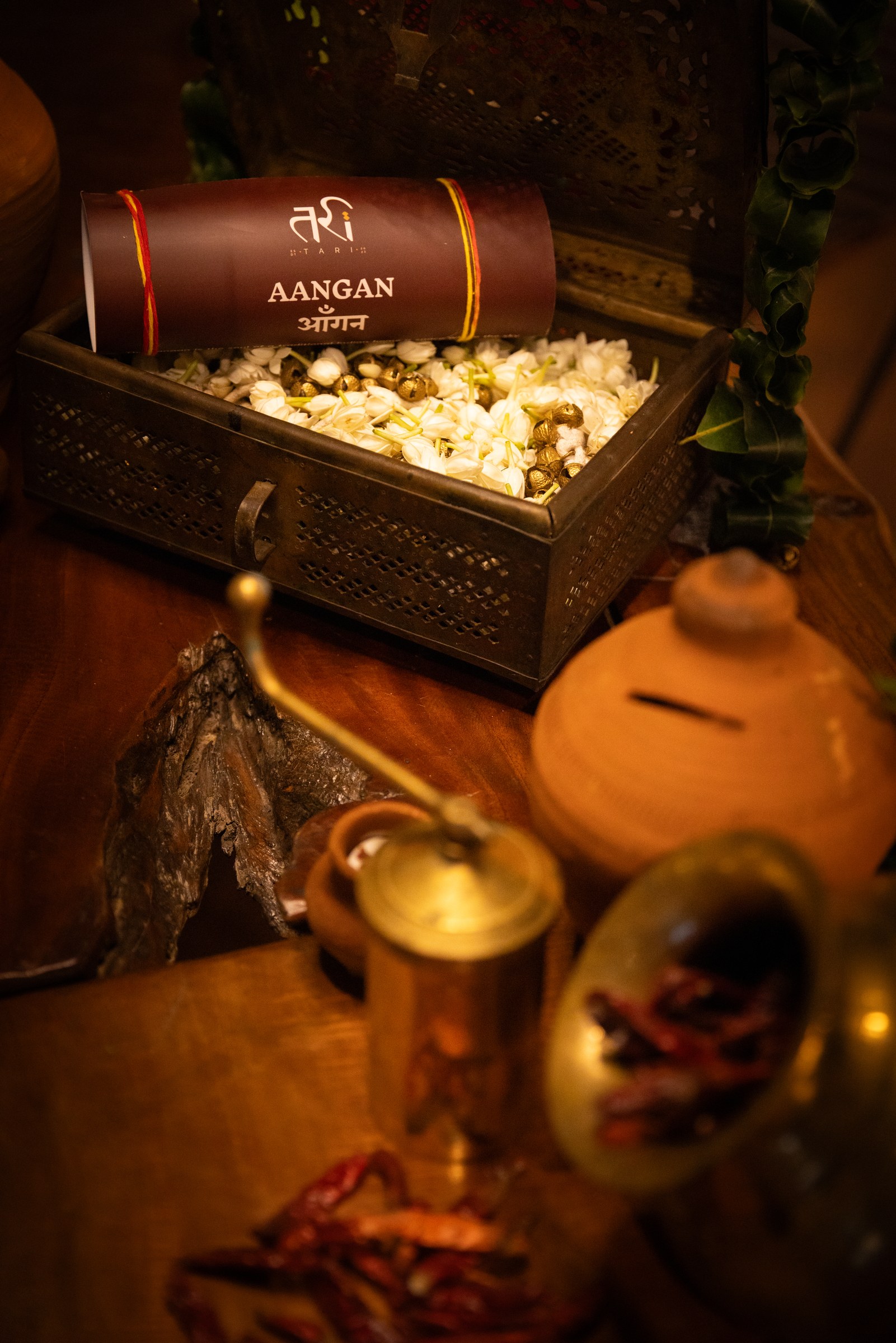 Brass box holding jasmine and gold seeds, the Aangan wordmark scroll at centre.