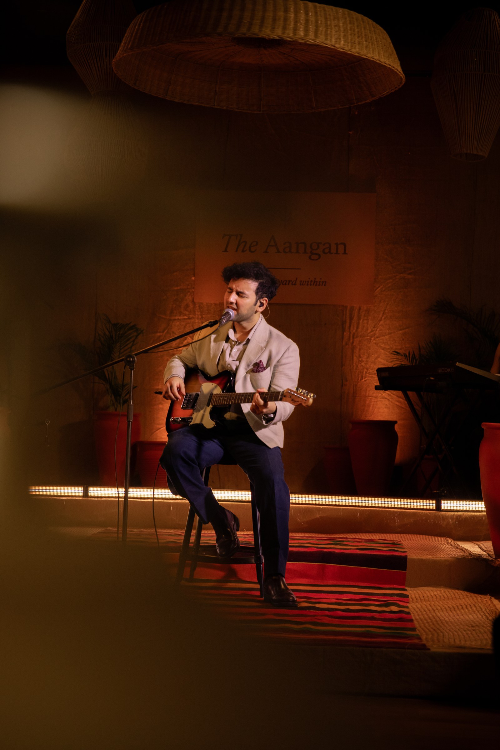 Viraj Bahri seated on stage at The Aangan, electric guitar in hand.
